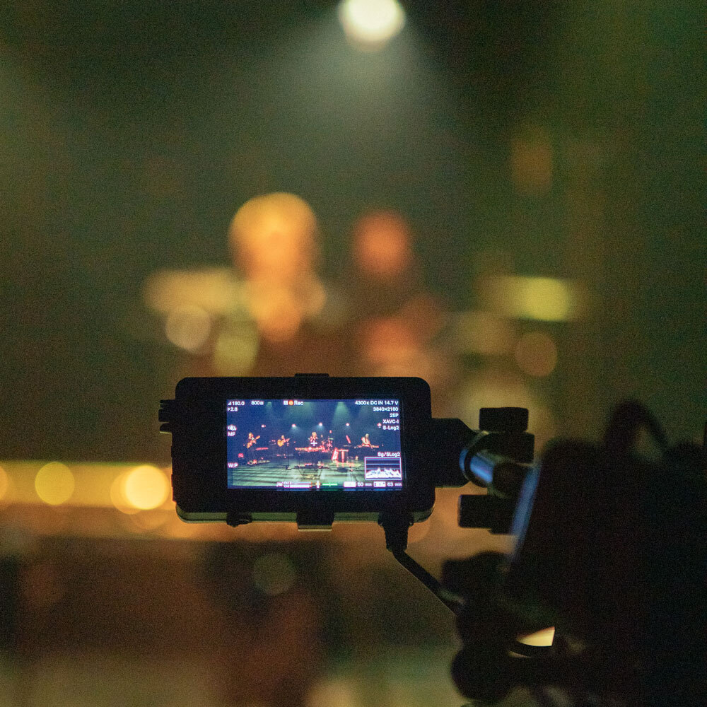 Eine Filmkamera filmt eine Band auf einer Bühne.