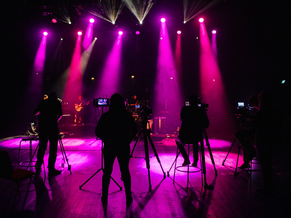 Ein Konzert wird auf einer Bühne mit lila Licht gefilmt.
