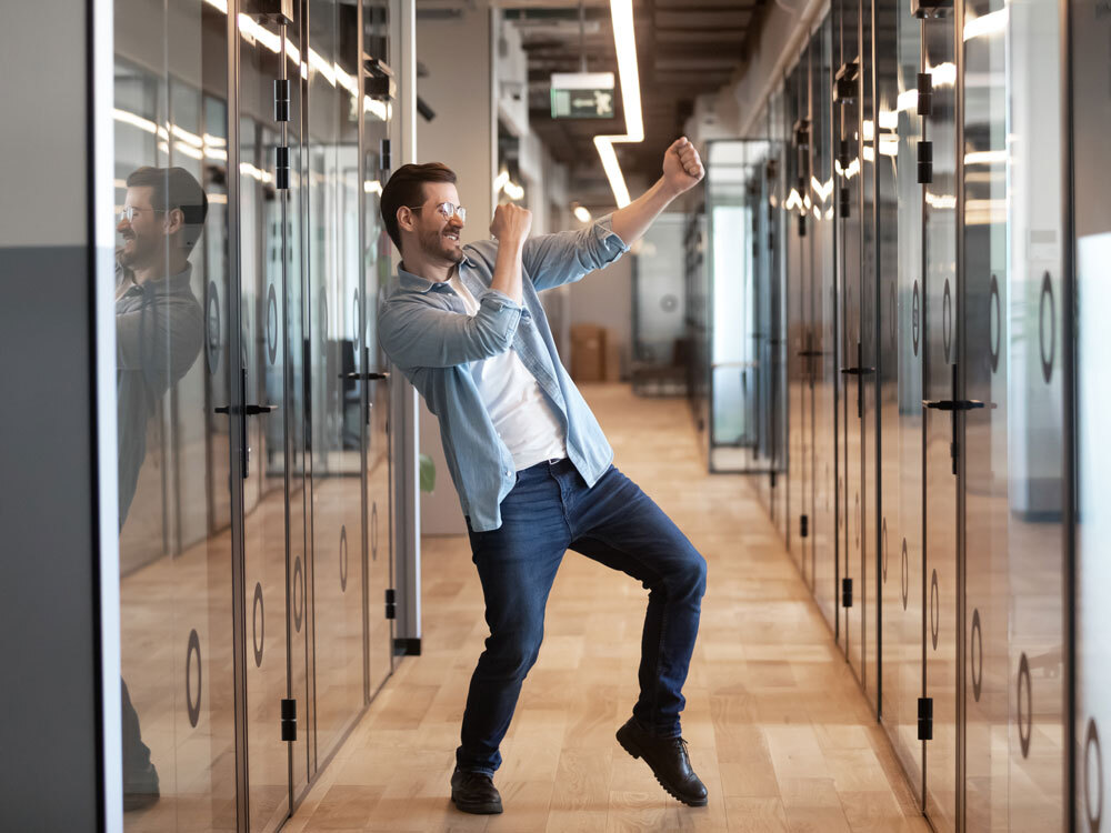 Junger Mann tanzt im blauen Hemd durch den Büro Flur.