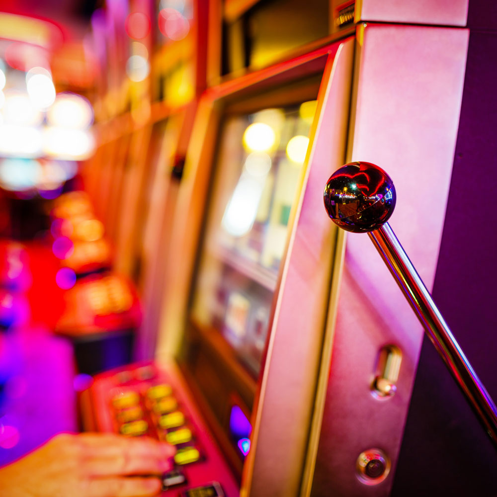 Der Spielautomat wird von einer Hand bedient, buntes Licht umgibt die Szenerie.