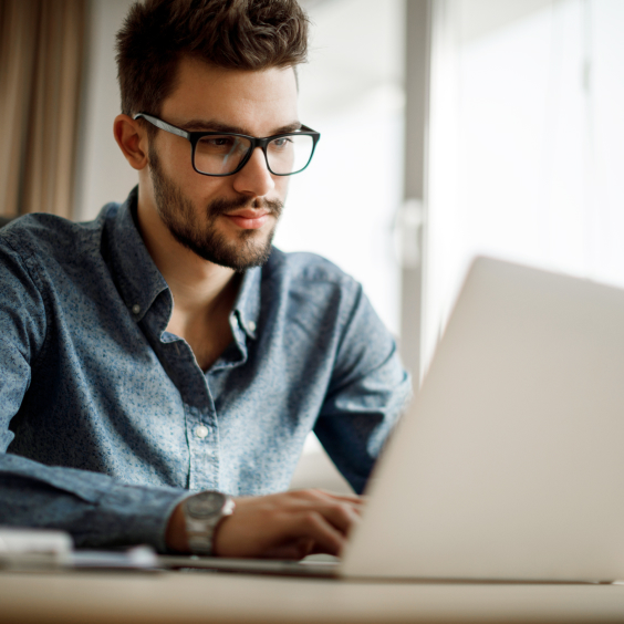 Ein junger Mann mit einer Brille sitzt vor seinem Laptop.