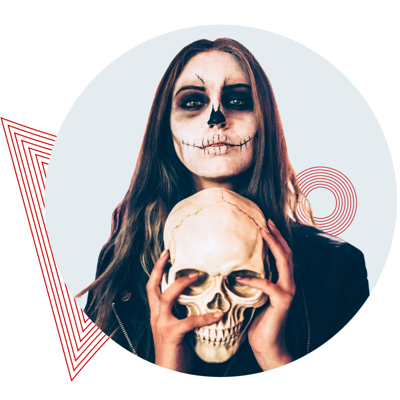Frau hält Totenkopf vor ihr Gesicht auf einer Halloween-Party mit mehreren Personen im Hintergrund.
