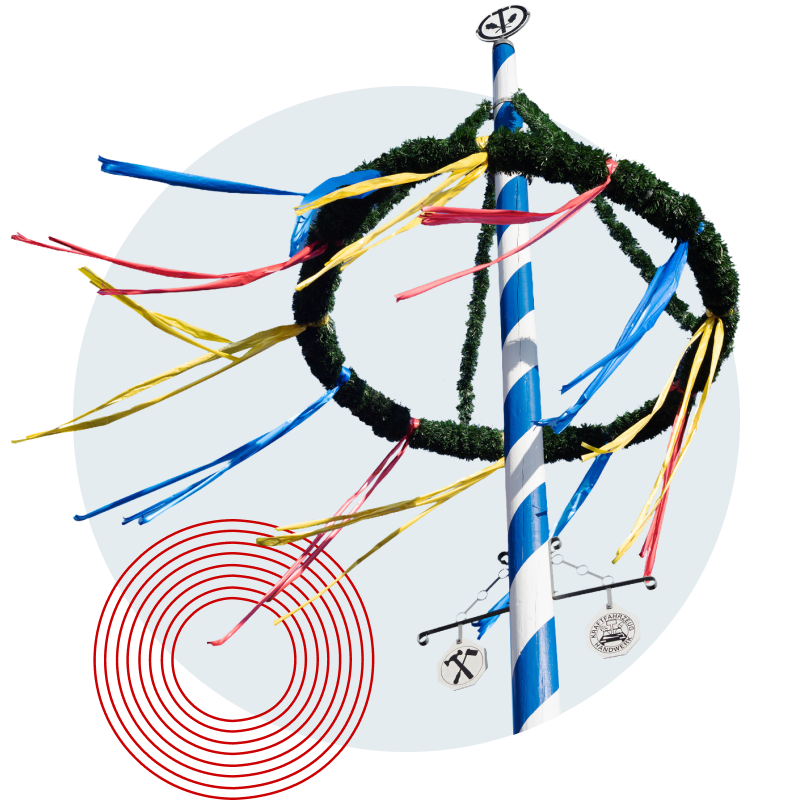 Maibaum mit blau-weißer Streifenbemalung, geschmückt mit einem grünen Kranz und bunten Bändern in Gelb, Rot und Blau.