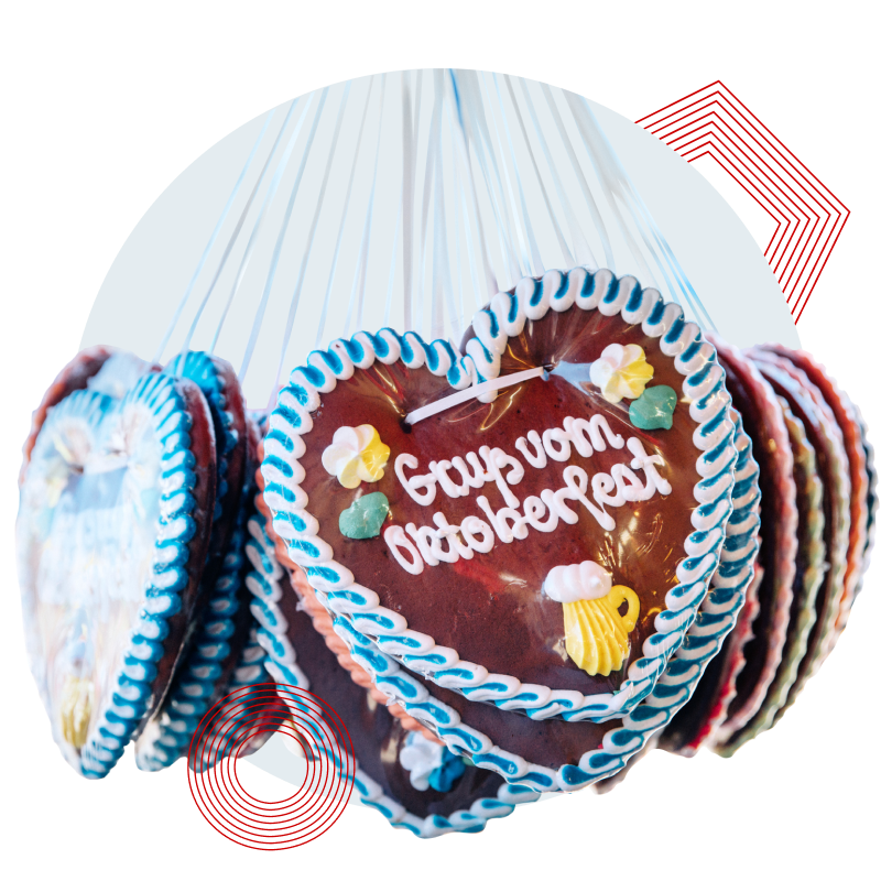 Mehrere Lebkuchenherzen mit Zuckerdekoration und der Aufschrift 'Gruß vom Oktoberfest' hängen an Bändern.