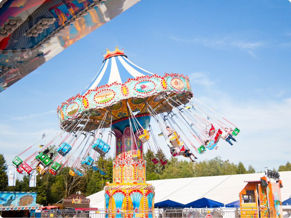Kettenkarussell mit bunten Sitzen, das sich vor blauem Himmel und Bäumen dreht.