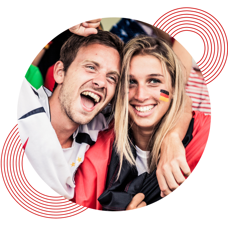 Zwei Personen mit Umhängen in den Farben der deutschen Flagge umarmen sich und feiern.