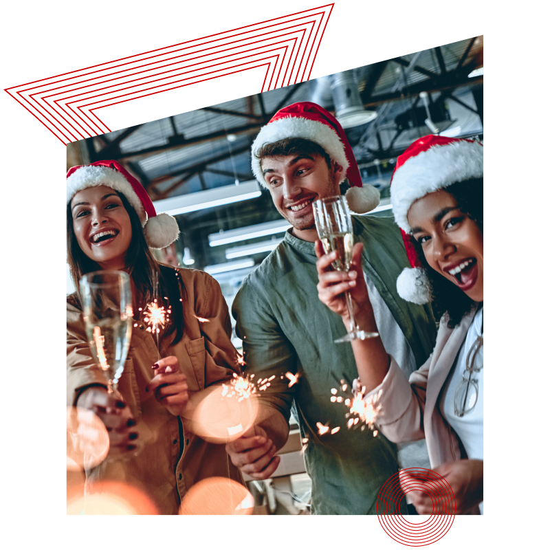 Gruppe von vier Personen mit Weihnachtsmützen, die Sektgläser und Wunderkerzen in einer festlich dekorierten Industriehalle halten.