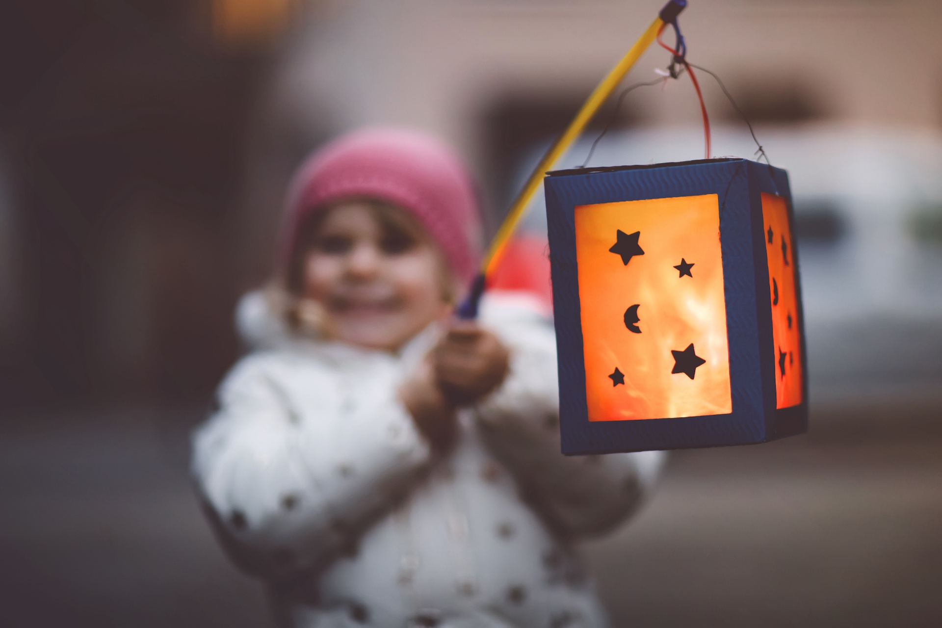 Kind hält Laterne mit ausgeschnittenen Sternen und Mondsichel an Stab.