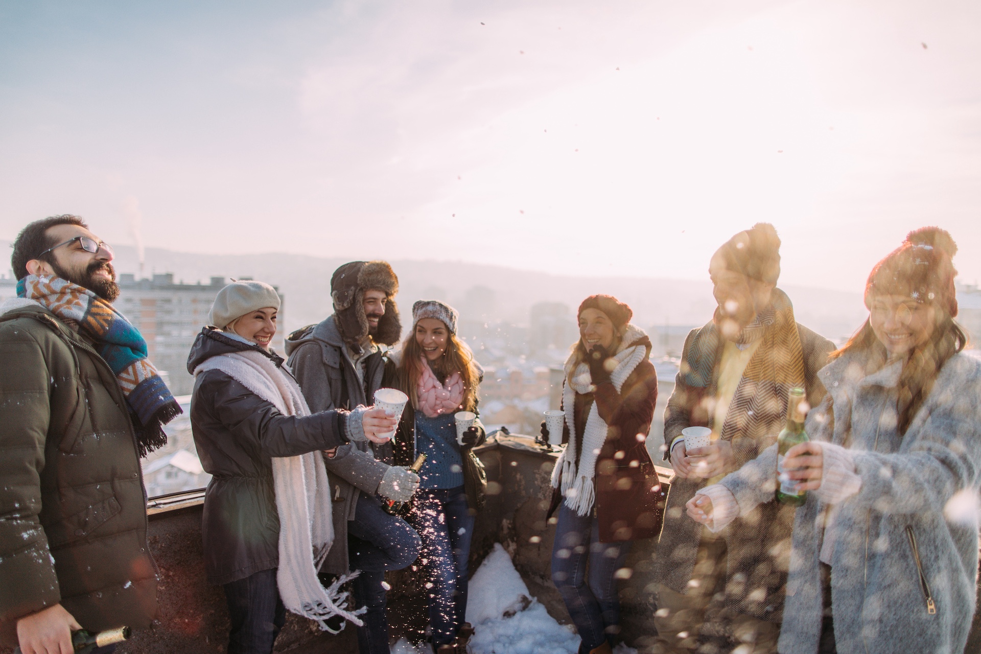 Gruppe von Menschen in Winterkleidung steht draußen auf einer Terrasse und hält Getränke in den Händen.