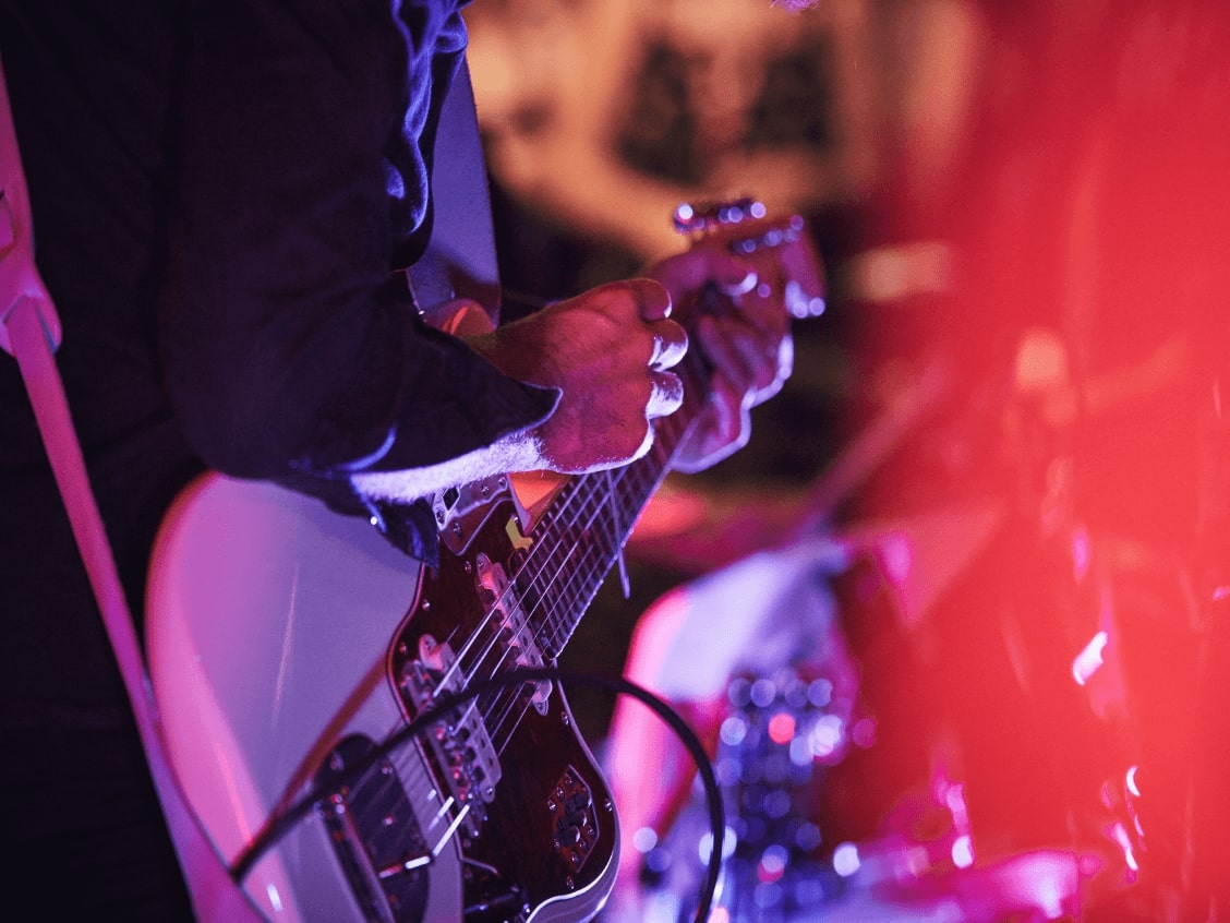 Eine Person spielt E-Gitarre in buntem Bühnenlicht.