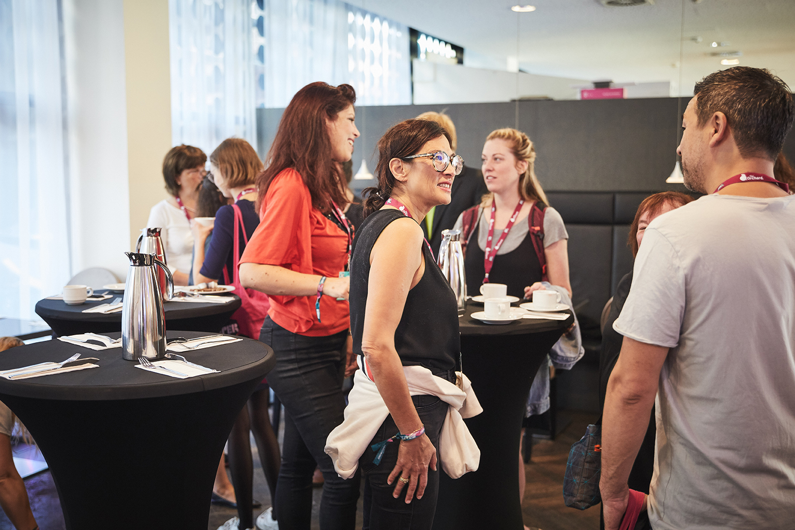 Menschen stehen und unterhalten sich bei einem Stehempfang mit Kaffeetischen und silbernen Kannen.