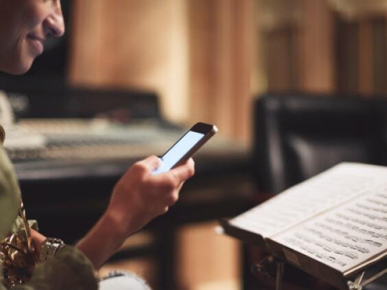 Person holding a mobile phone, sitting in front of a music stand with sheet music in a music studio.