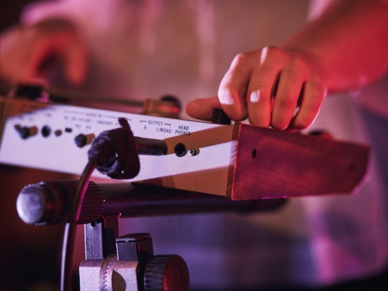 Hände bedienen ein elektronisches Musikinstrument auf einem Ständer.