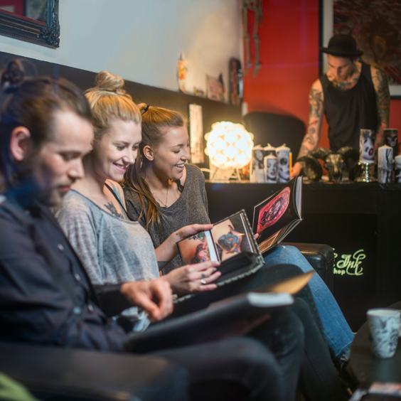 Mehrere Personen sitzen gemeinsam in einem Tattoostudio.