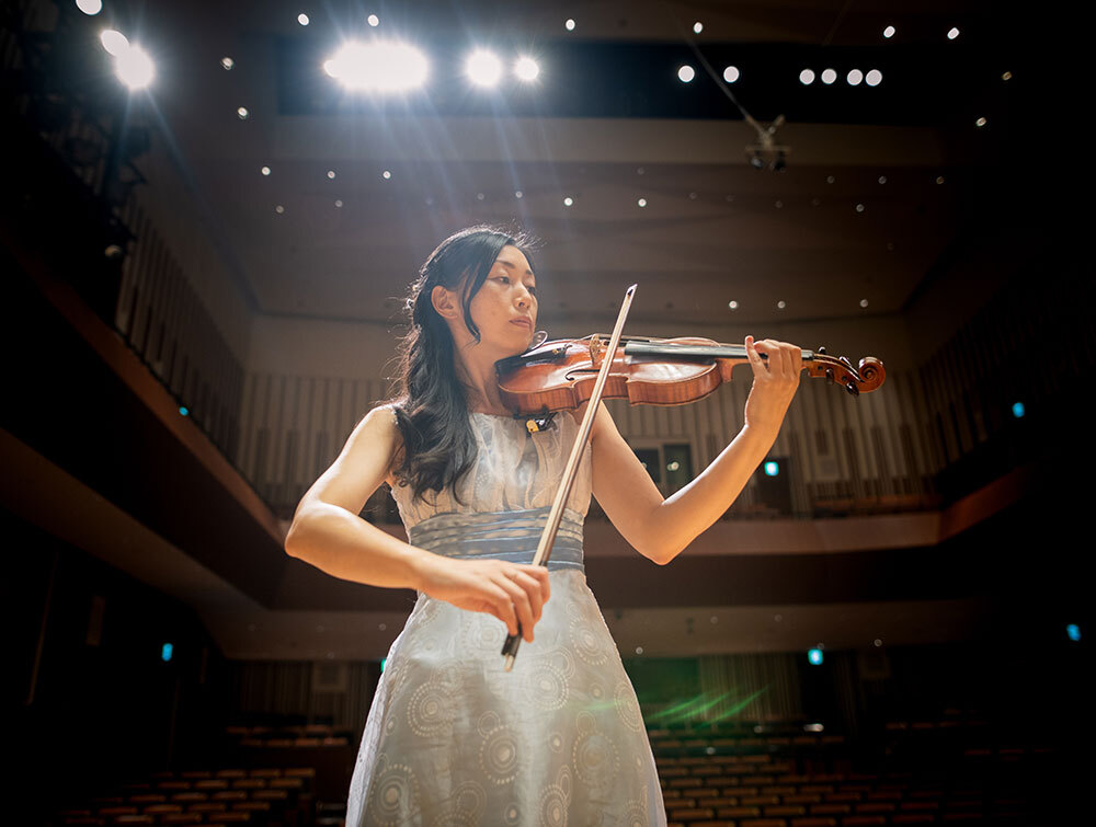 Eine Frau steht in einem Konzertsaal und spielt Geige im weißen Kleid.