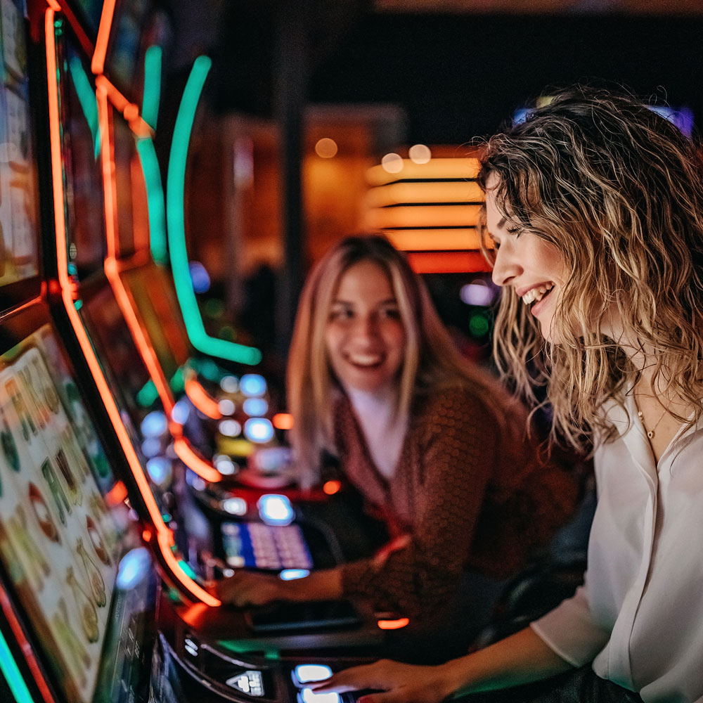 Zwei fröhliche Frauen spielen an bunten Spielautomaten in einer Spielhalle