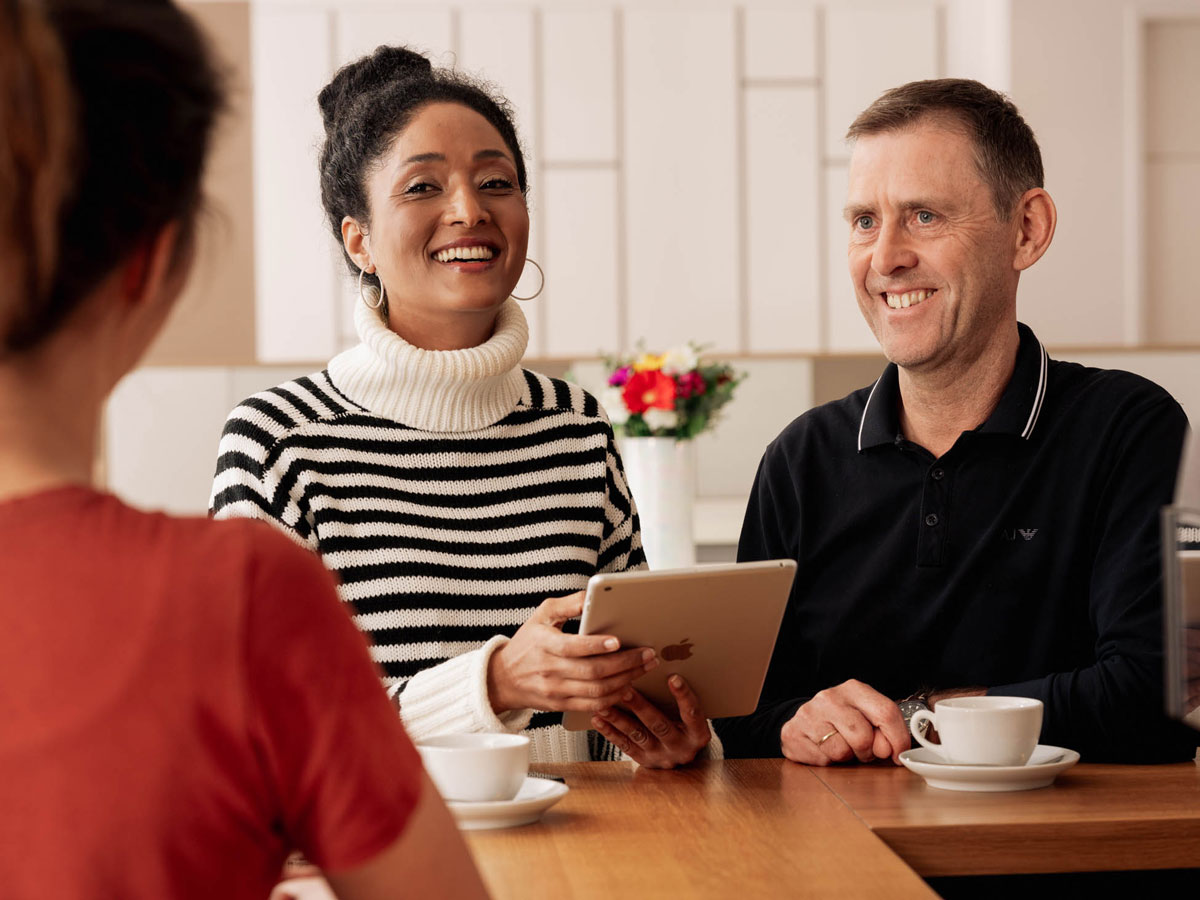 Woman with iPad talks to man drinking coffeeFrau mit iPad unterhält sich mit Mann in Kaffeebar