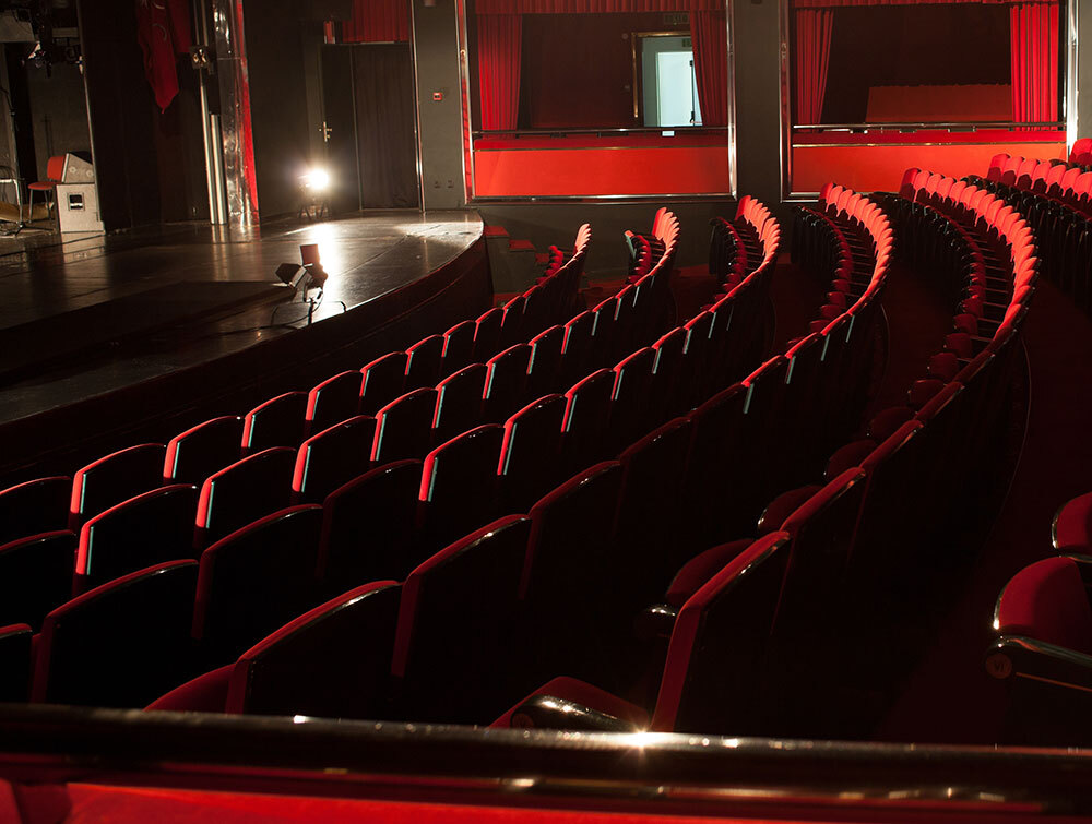 Ein leerer Theatersaal mit roten Stühlen.