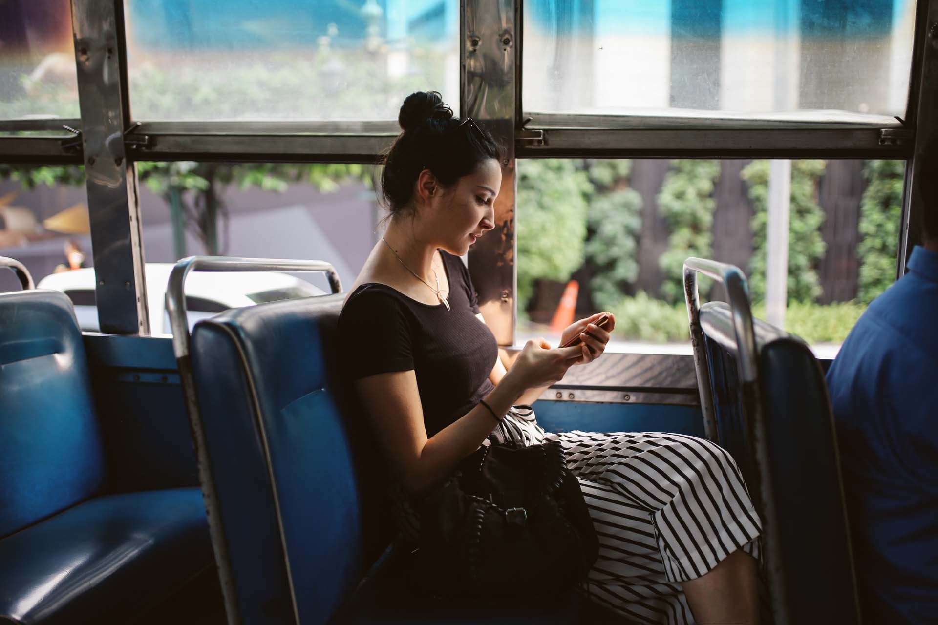 Frau sitzt im Bus und schaut auf ihr Handy