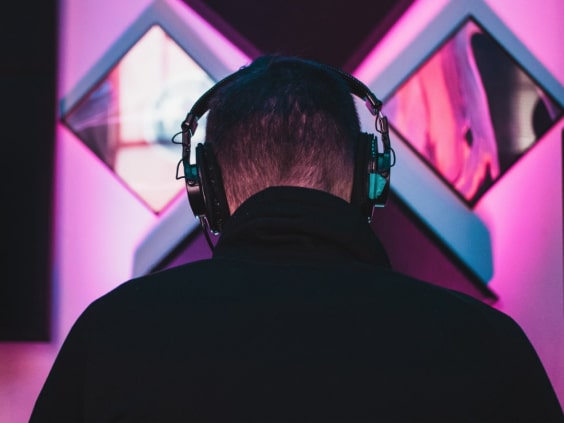 MusicHub DJ sitzt mit Kopfhörern mit dem Rücken zugewendet an seinen Arbeitsplatz