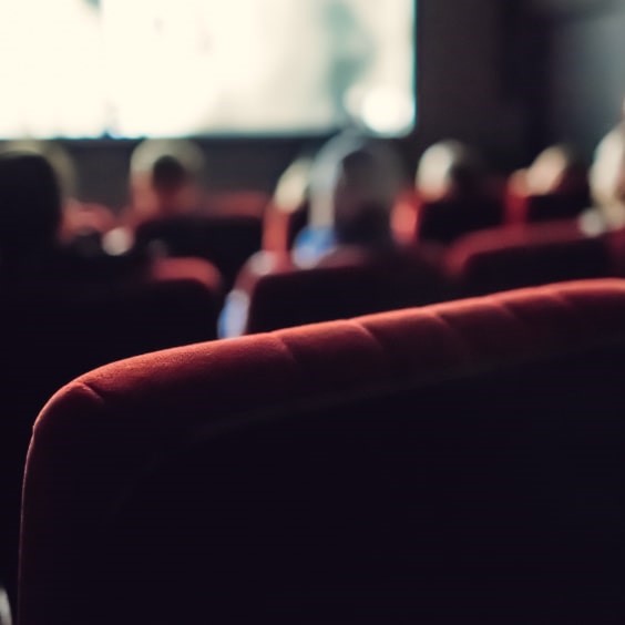 Ein leerer Stuhl im Kinosaal mit sitzenden Personen im Hintergrund